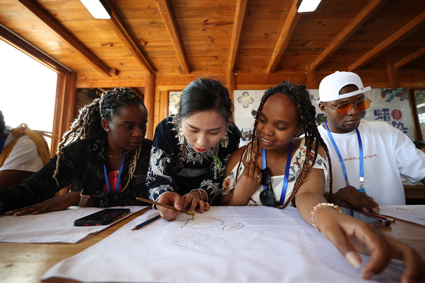 7月21日，非遺傳承人張義蘋（中）在向留學生示范苗族蠟染繪畫技藝。