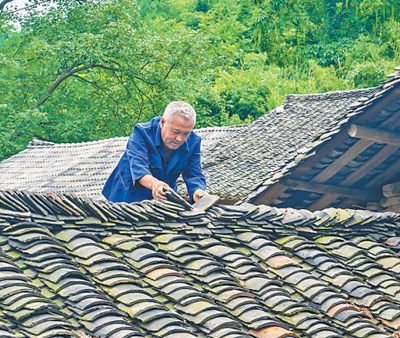圖為萬明春在撿瓦，修補漏雨的地方。蘇 濱 涂 敏攝影報道