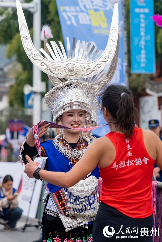 身著苗族盛裝的工作人員為完賽運動員佩戴紀念品。人民網記者 涂敏攝