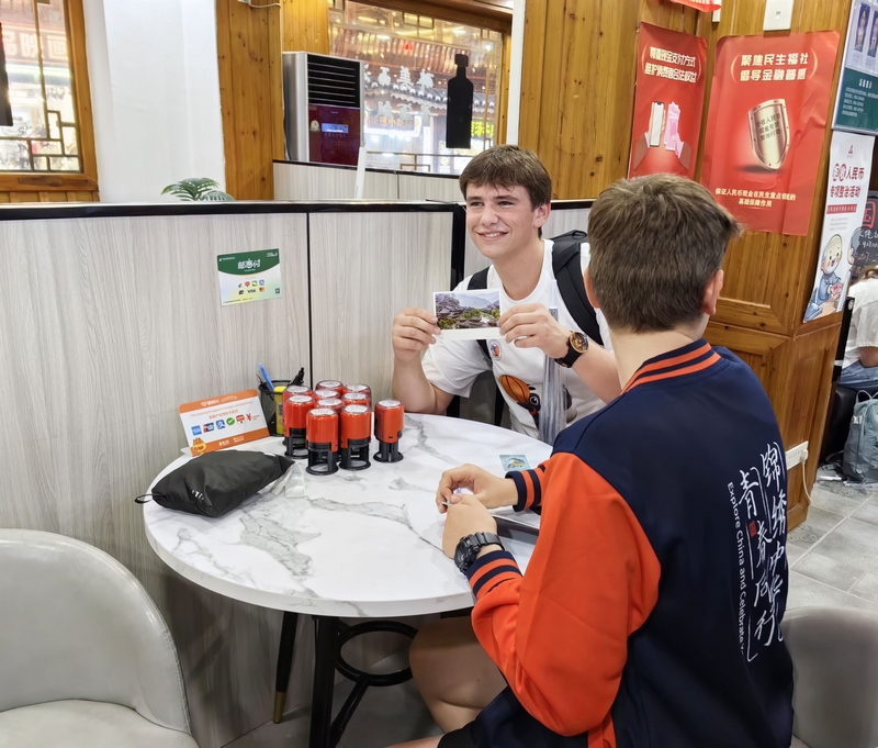 外國游客在西江千戶苗寨景區通過移動支付購買蓋有西江郵政郵戳的明信片。